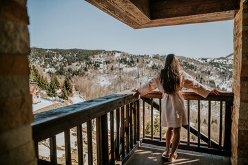 Charming young woman in bathrobe enjoying the winter nature on the large terrace