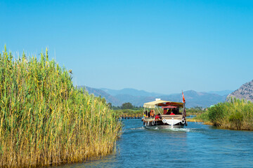 Fototapeta premium Tourist pleasure boat on the Dalyan River, next to the rocks, which contain the Lycian tombs, in Mugla Province located between the districts of Marmaris and Fethiye on the south-west coast of Turkey