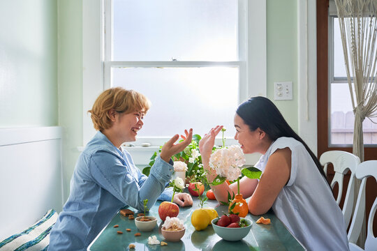 two women smile at table with fruit and flowers