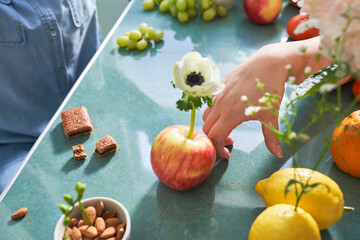 hand rests on table with fruit and flowers
