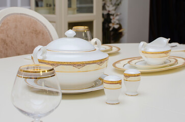 Plates, a tureen, a glass and other utensils are on the table. Beautiful tableware in a classic style.