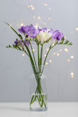 bouquet of twigs of delicate purple and white freesia flower in a glass bottle on a gray background