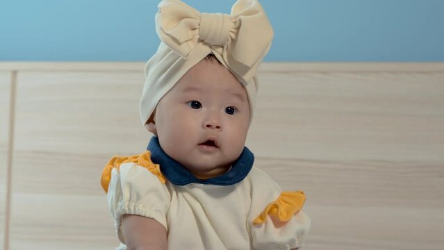 4K 25fps Slow Motion, A newborn girl, big round eyes, cute face, wearing cute clothes, wearing a hat with Boze on her head, sitting with big eyes looking at something interesting.