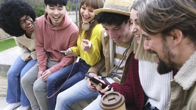 Group of millennials people laughing using smart mobile phone outside - University students having fun together in college campus - Youth lifestyle concept