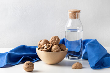 Still life with walnuts lying in a wooden bowl, a carafe of water and a blue towel.