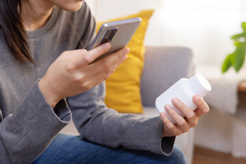 Asian Woman Read Medicine Prescription on Her Mobilephone While Holding Pills Bottle on the Sofa