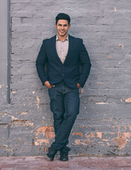 Success looks this good. Portrait of a handsome young businessman standing against a face brick wall with his hands in pockets.