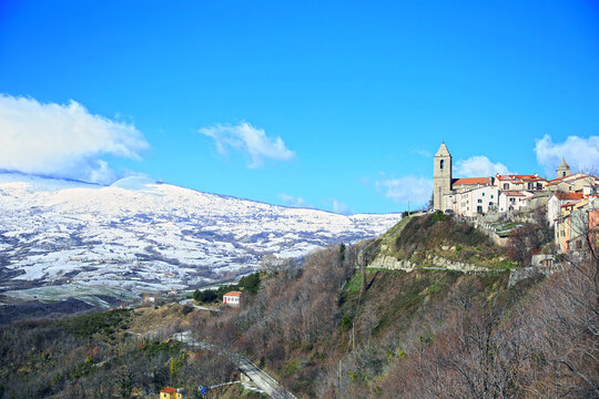 A glimpse of the village of Agnone, nestled among the snow-covered mountains, against the crystal clear blue sky, Agnone, Molise, Italy