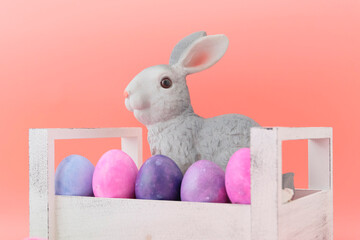 Beautiful pink tulips, rabbit toy and Easter eggs, pink, blue, light blue in a wooden white box. Pink background. Concept illustration of Easter, holiday. Greeting card. Close-up