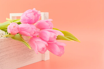 Beautiful delicate top bouquet of live spring pink tulips in a wooden light box on a pink background. The concept of flowers for the holiday. Greeting card.