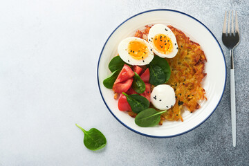 Breakfast. Potatoes latkes with sour cream, spinach salad, tomatoes and boiled eggs on light background.  Delicious food for breakfast. Top view.