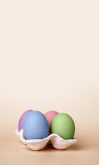 Banner with multicolored Easter eggs in carton box on beige background. Symbol of religious holiday. Copy space. High quality photo