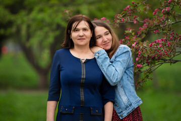 young woman and her adult daughter are walking in a spring park among flowering trees - 495741871