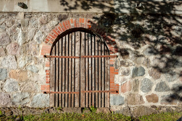 Masonry. Fragment of a wall from a large stone with old wooden gate and the shadow of the tree. Brown stone. Close-up.