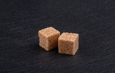 Two pieces of refined cane sugar on a dark background.