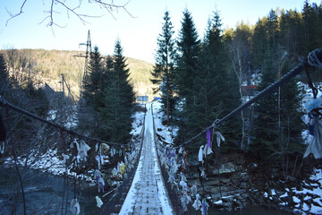 Low angle of a suspension bridge with handkerchiefs tied on both sides in a pine forest