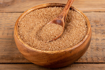 Close-up of a wooden spoon and a wooden bowl with cane sugar.