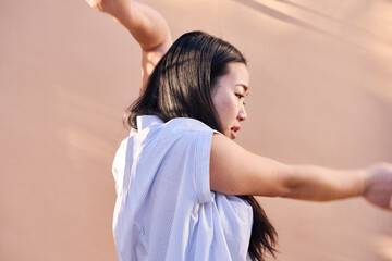 profile of woman dancing by wall with arm raised