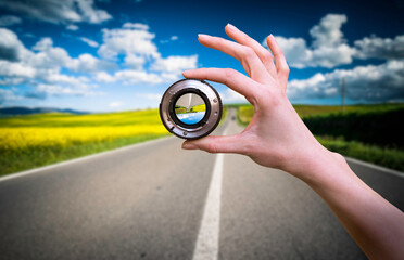 Hand holds lens against road in the nature at spring.