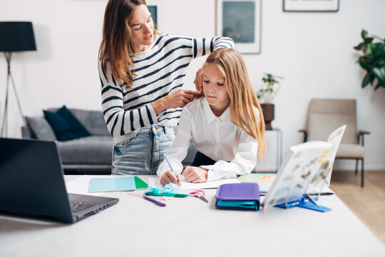 Girl is doing her homework while her mother brushes her hair