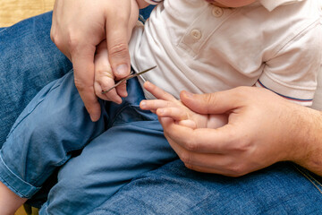 Dad with a little child kid baby cutting nails close up. Son on his father's laps in the couch at home. care, paternity, family concept