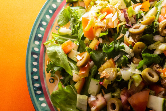 Detalhe de prato com salada de vegetais sobre superfície alaranjada.