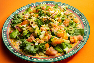 Detalhe de prato com salada de vegetais sobre superfície alaranjada.