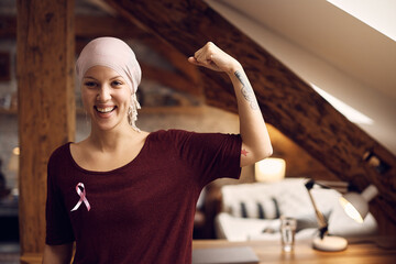 Happy breast cancer survivor flexing her muscle at home and looking at camera.