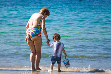 senior woman on sea shore at beach with little child