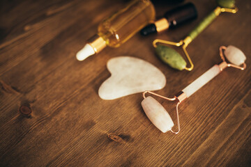 Jade rollers and face massagers and natural oil in bottles on wooden background. Skin care.