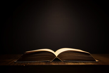 image of open antique book on wooden table with dark background