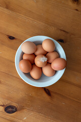 A  flat lay style image of a bowl of eggs on  a wooden style background with a feather on the top egg