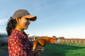 Closeup shot of a Hispanic girl with a hen looking at the landscape and smiling in New Zealand