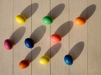 Many colored Easter eggs on wooden background, with sunlight and shadows, top view