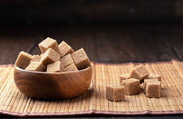 Refined cane sugar cubes in a wooden bowl on a mat.
