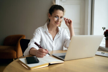 A freelance woman with glasses designer uses a laptop online on the website, works in a modern cozy office