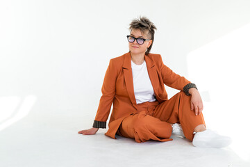 young emotional non binary person wearing orange color suit posing at studio