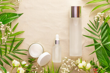 Fototapeta na wymiar Glass cosmetic bottles, open cream jar, tropic plants and flowers