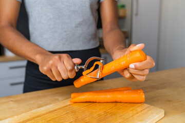 Detailed shot of a male peeling carrot on a wooden cutting board.