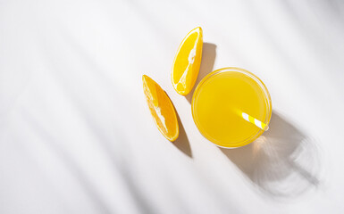 A glass of orange juice and a slice of orange on a light  table with palm leaf shadow. Summer time. Top view and copy  space