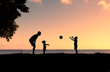 silhouette of father and children playing game with ball outdoors in the park. Fatherhood, and...