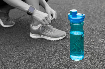 Drink water health concept  Female runner tying her shoe next to bottle of water