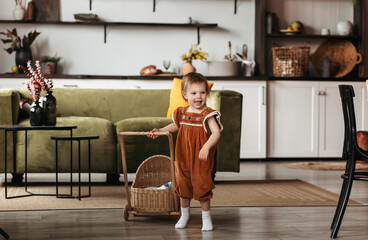 Happy little girl is playing with a stroller in the children's room. Little girl is playing with a...