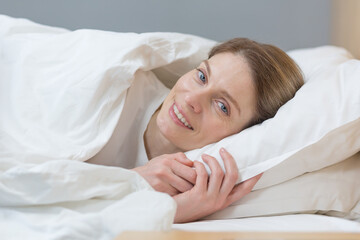 Fototapeta na wymiar Close-up photo of portrait of woman sleeping in bed smiling and looking at camera in the morning