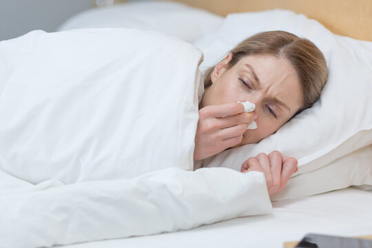 Close-up photo of a sick woman lying under a blanket in bed at home, has a runny nose and cold