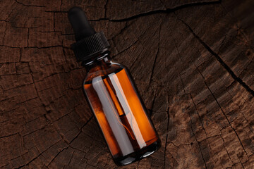 Empty mock-up of medical bottle for oil. Transparent amber glass bottle on wooden background. Concept of herbal medicine, top view.