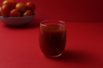 red tomato juice in a glass next to tomatoes lie on a plate on a red background with a place for text. Healthy Food Drinks Vitamins