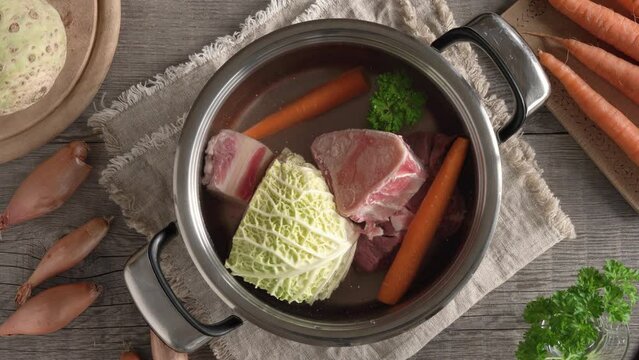 Preparation of homemade broth or soup - putting a carrot into a pot with water, bones beef meat and fresh vegetables