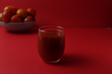 red tomato juice in a glass next to tomatoes lie on a plate on a red background with a place for text. Healthy Food Drinks Vitamins