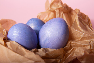 Purple painted shiny Easter eggs in brown craft paper on a pink background